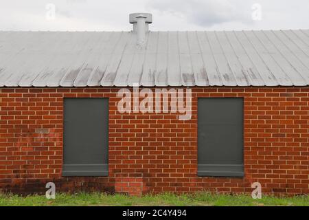 a pair of grey painted over windows against a red brick warehouse building Stock Photo