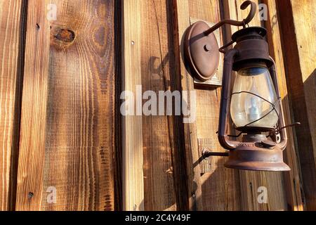 a rusted old gas lantern hanging on an old log cabin shed building Stock Photo