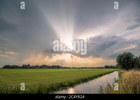 Sunbeams shine through the clouds of a thunderstorm during sunset Stock Photo