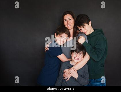 Mother with three older boys hugging against black backdrop. Stock Photo