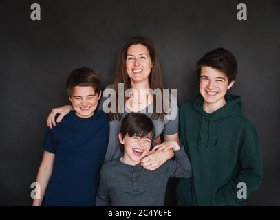 Mother with three older boys laughing against black backdrop. Stock Photo