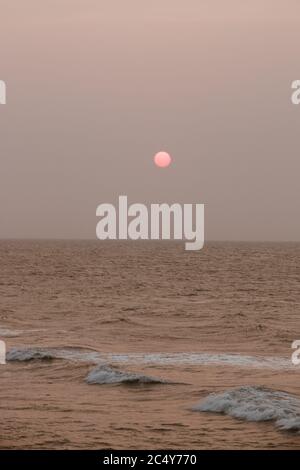 A bright pink full moon rises over a rough sea in Cartagena after dusk Stock Photo