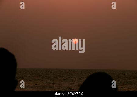 A full red moon rises above the ocean between two silhouetted heads Stock Photo