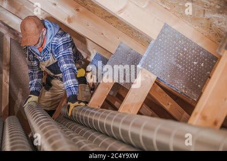 Male Ventilation Technician Installing New Air Vent System In Attic Of Residential Building. Stock Photo