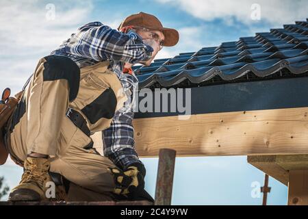 Close Up Of Male Contractor Near Roof Covered With Black Ceramic Tiles Talking On Cell Phone. Stock Photo