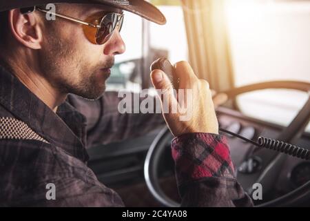 Caucasian Male Truck Driver Sitting In Cab Of Vehicle Talking On Two Way Radio. Stock Photo
