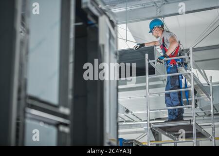 Construction Worker Checking Newly Installed Air Ventilation Shaft On Ceiling Of Large Commercial Building. Stock Photo
