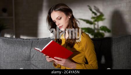Pretty young woman is reading a book at home Stock Photo