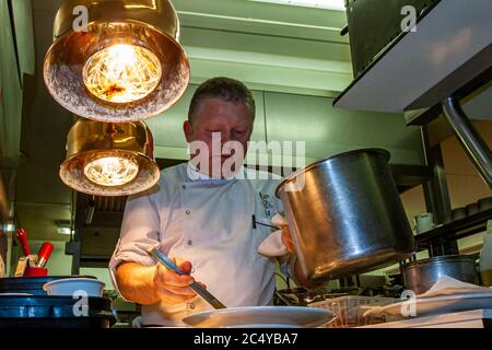 Star chef Loïc Le Bail holds a steaming pot and plates a dish with tongs, in the kitchen of Hotel Brittany & Spa, Roscoff, Brittany, France. Stock Photo