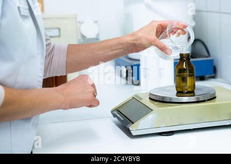 A close up of a female pharmacist mixing chemical liquids on medical scales in a laboratory Stock Photo