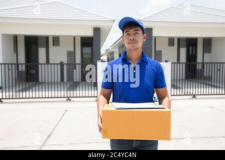 Asian delivery servicemen wearing a blue uniform with a bluecap and  handling cardboard boxes to give to the female customer in front of the house. On Stock Photo