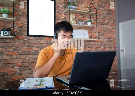 Asian businessmen is using notebook computers and wear headphones for online meetings and working from home. Stock Photo