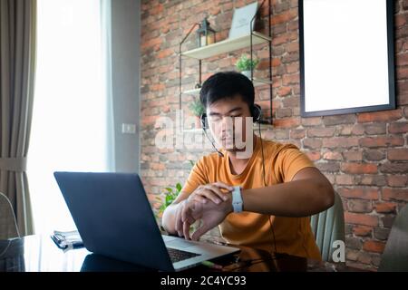 Asian man is watching the time and he uses a notebook computer to work at home. Stock Photo
