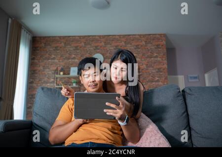 Asian Couple shopping online and paying with credit card at laptop computer,Happy couple at home surfing the net on sofa Stock Photo