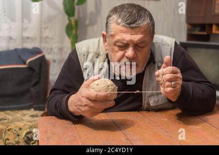 Indoor portrait of senior Ukrainian peasant taking clew of thread while sitting at old table Stock Photo
