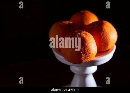 Four tangerines lie on a white stand. Black background. Concept photo. Stock Photo