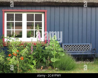 Wooden wall with window, bench and flowers in the garden Stock Photo