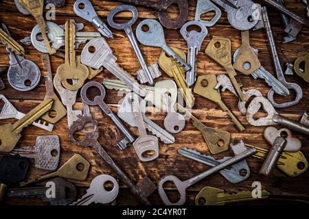 Many assorted old multi-colored metal antique keys of different shapes on wooden scratched table background. Home security concept. Stock Photo