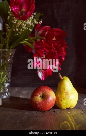 Red tulips and lizards in a vase and apple with pear on a black background Stock Photo