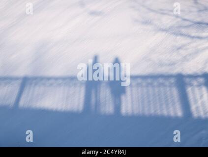 Shadow silhouette of couple man and woman standing on a bridge on snow background on sunny winter day Stock Photo