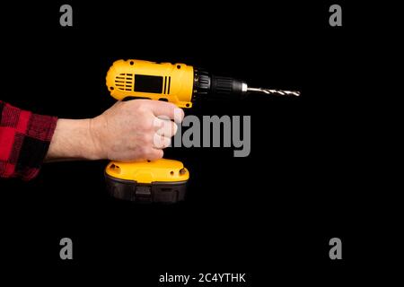 a worker in a red plaid shirt uses an electric drill isolated on black Stock Photo