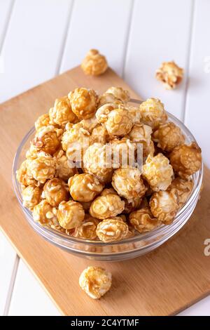 Sweet caramel popcorn in glass bowl. Close up. Light wooden background. Stock Photo