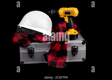 a yellow electric drill with a red plaid worker shirt and a white hard hat on an aluminum equipment case isolated on black Stock Photo
