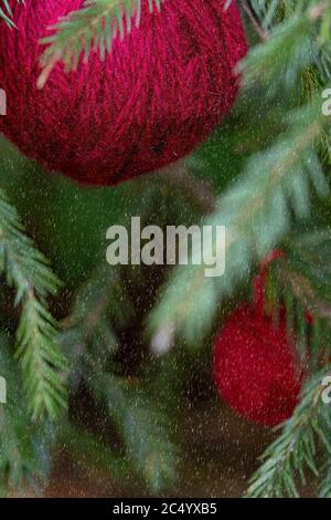 Christmas background with balls of yarn. Red wool balls hanging on the green branches of a Christmas tree. with Vertical poster with copy space. The c Stock Photo
