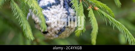 Christmas background with balls of yarn. White with blue wool ball hanging on the green branches of a Christmas tree. Horizontal banner with copy spac Stock Photo