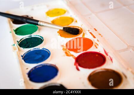 The palette of watercolor paint and one brush on white sheets of paper Stock Photo