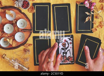 Wiccan witch reading the future at her altar using 5 card tarot spread on bright yellow cloth (flat lay) Hand painted Death tarot card holding in hand Stock Photo