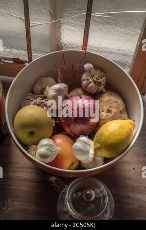 A still life of a bowl of mixed fruit and vegetables sitting on a counter top in a kitchen. Stock Photo