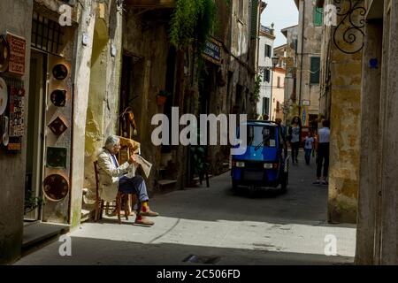 Street scene with a man reading the newspaper and an approaching Piaggio, sometimes referred to as Ape Piaggio, Apecar, Ape Car or just Ape, which is Stock Photo