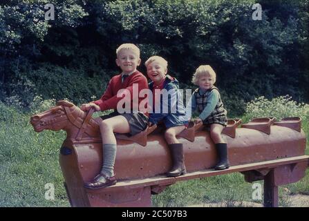 1967, three young children playing or riding on a brown coloured metal five seater rocking horse outside in a park, Surrey, England, UK. This type of traditional, possibly victorian, play equipment was to be found in playgrounds and public parks across Britain in this era and young children had enormous fun playing on them as can be seen by the big smilies in the picture. Stock Photo