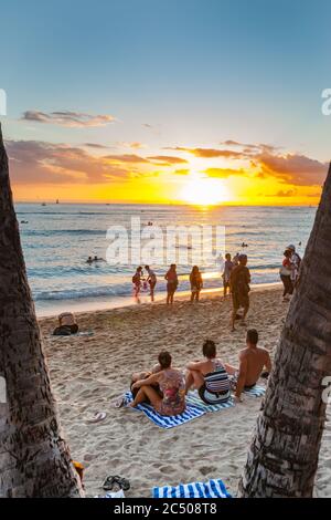 Hawaii USA - November 8 2014; Tourists enjoying tropical beach and sunset between palm tree trunks on island paradise. Stock Photo