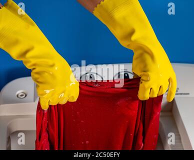 girl hands with yellow cleaning gloves taking out a shirt from washing machine and blue background Stock Photo