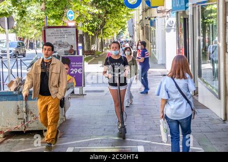 Jaen, Spain - June 18, 2020:  Young woman riding an electric scooter by the sidewalk wearing a protective mask. Stock Photo