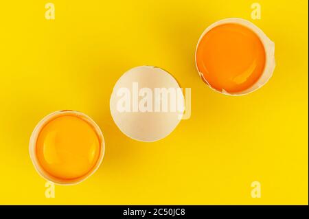 Raw egg yolks in the halves of cracked brown eggshells on yellow background. Diagonal line Stock Photo