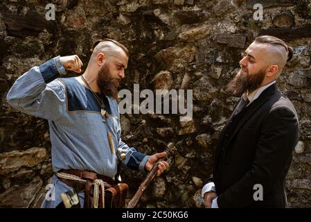 A man in Viking clothes challenges his alter ego who derides him in contemporary clothes, the same man face to face in clothes from different eras Stock Photo