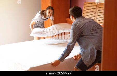 Young couple making bed together. Concept of making the bed as a couple. Millennial family. Stock Photo