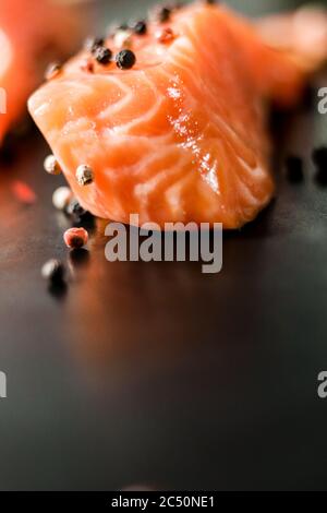 Raw sea red salmon fish fillet uncooked piece with colorful peppercorns on black background. Stock Photo
