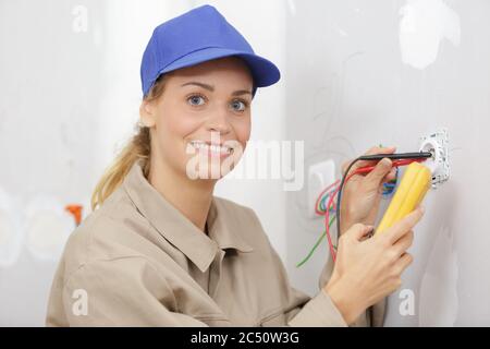 happy female electrician fixing electric cables in socket Stock Photo