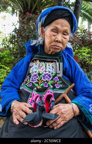 Kunming, China - June 24, 2019: Portrait of a Chinese woman holding her small shoes. She had her feet bound (footbinding) also called Lotus Feet Stock Photo