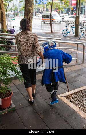 Kunming, China - June 24, 2019: Chinese woman that had her feet bound (footbinding) also called Lotus Feet walking away from the camera Stock Photo