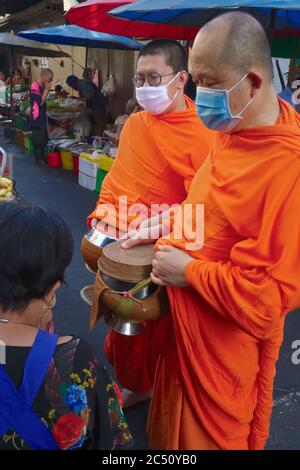Two Buddhist monks wearing anti-Covid masks are given alms during their daily early morning alms round (binta baat) in a market in Bangkok, Thailand Stock Photo