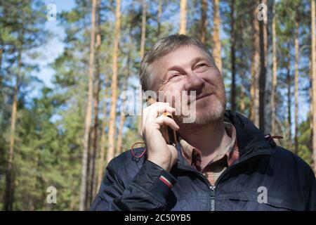 A middle-aged man smiles and talks on the phone in the park. A clear sunny day. Good mood. Stock Photo