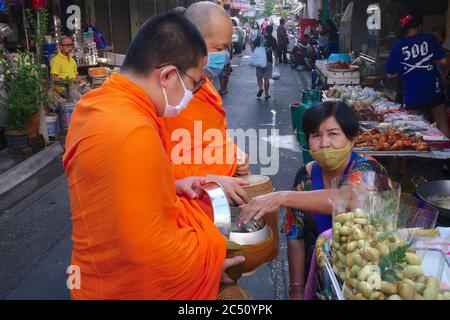 Two Buddhist monks wearing anti-Covid masks are given alms during their daily early morning alms round (binta baat) in a market in Bangkok, Thailand Stock Photo