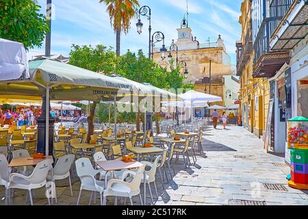 SANLUCAR, SPAIN - SEPTEMBER 22, 2019: The alley along the tables and sunshades of cozy outdoor cafes, located in Plaza del Cabildo square, on Septembe Stock Photo