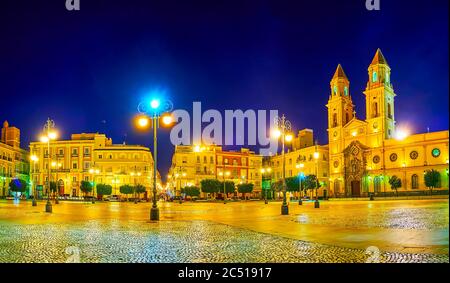 Panorama of the evening Plaza de San Antonio square with tall belfries of St Anthony of Padua church, historic edifices and vintage streetlights, Cadi Stock Photo