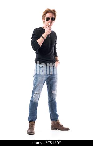 Cool attitude stylish young man with sunglasses lighting up cigarette with lighter. Full length portrait isolated on white background. Stock Photo